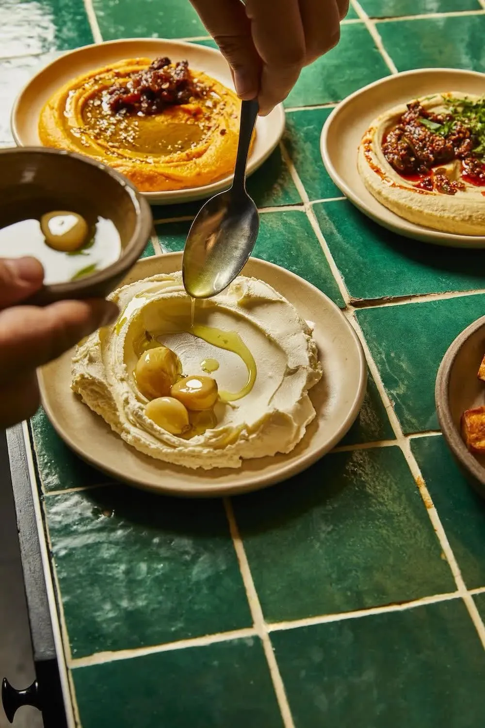 Hummus, muhammara, and dips with olives on a green tiled table